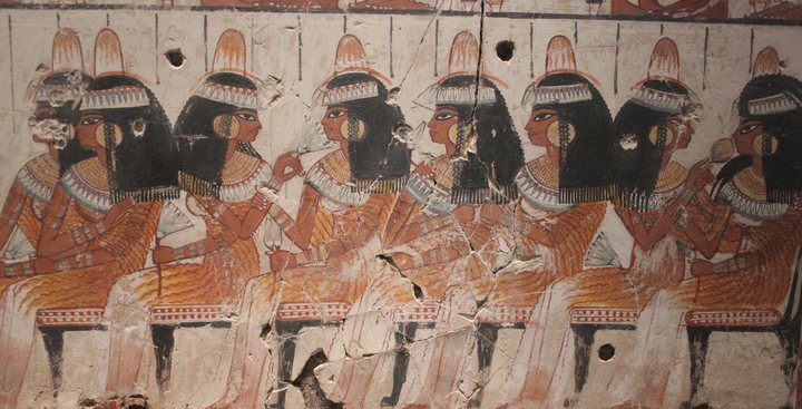 Pintura egípcia de um banquete: convidadas sentadas lado a lado, com cones perfumados sobre as perucas e flores de lótus nas mãos.